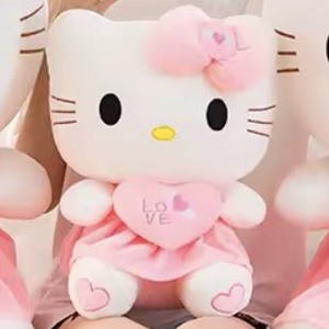 Puede incluir: Un peluche blanco con forma de gato con ojos negros, bigotes y nariz amarilla. Lleva un lazo rosa, un vestido rosa en forma de coraz&oacute;n con la palabra "LOVE" y detalles en forma de coraz&oacute;n en los pies. El juguete es suave y tierno.