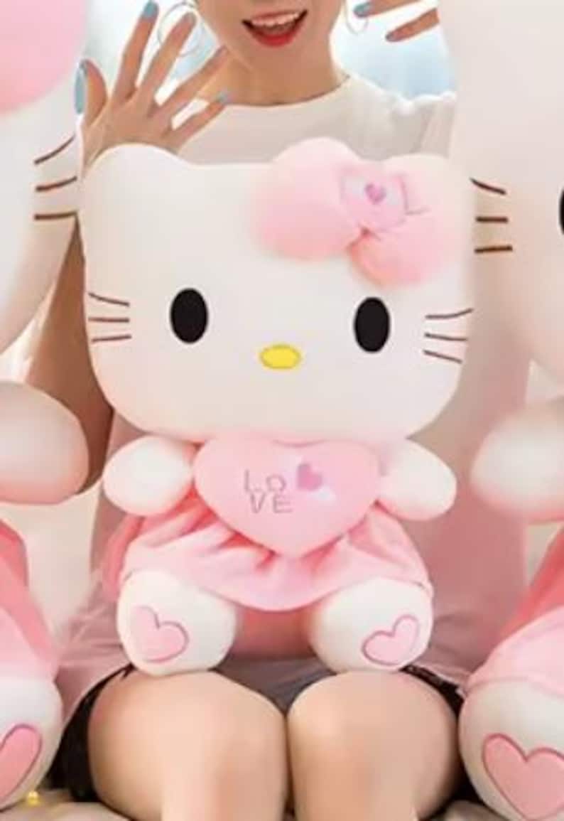 Puede incluir: Un peluche blanco con forma de gato con ojos negros, bigotes y nariz amarilla. Lleva un lazo rosa, un vestido rosa en forma de coraz&oacute;n con la palabra "LOVE" y detalles en forma de coraz&oacute;n en los pies. El juguete es suave y tierno.