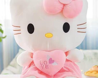 Puede incluir: Un peluche blanco con forma de gato con lazo rosa, vestido y detalle de corazón. El corazón tiene la palabra "LOVE" y un diseño de corazón alado. El gato tiene ojos negros, nariz amarilla y bigotes marrones. Juguete para niños.