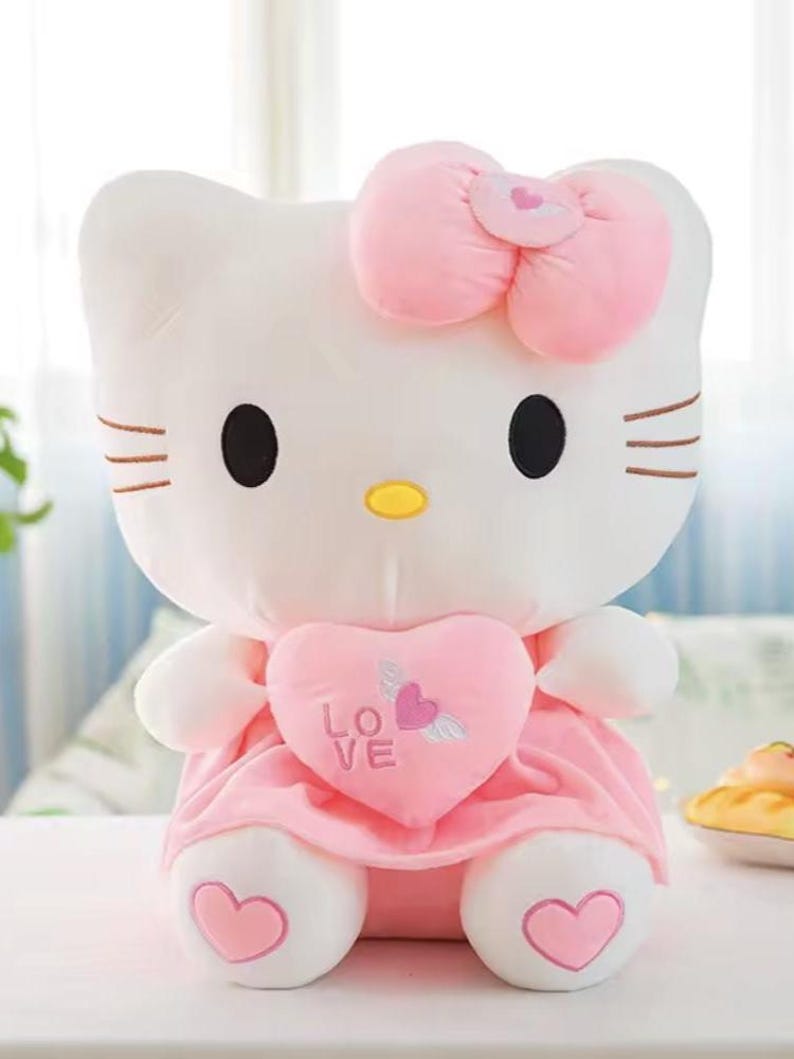 Puede incluir: Un peluche blanco con forma de gato con lazo rosa, vestido y detalle de coraz&oacute;n. El coraz&oacute;n tiene la palabra "LOVE" y un dise&ntilde;o de coraz&oacute;n alado. El gato tiene ojos negros, nariz amarilla y bigotes marrones. Juguete para ni&ntilde;os.