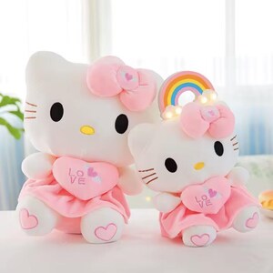 Puede incluir: Dos mu&ntilde;ecos de peluche blancos con forma de gato con lazos y vestidos rosas. Los mu&ntilde;ecos tienen ojos negros, narices amarillas y detalles de coraz&oacute;n rosa. Un mu&ntilde;eco tiene un arco&iacute;ris y luces. Un juguete lindo y tierno.