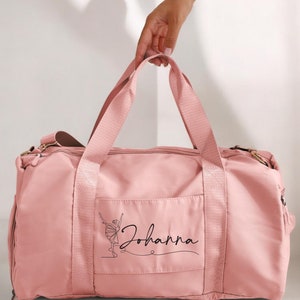 May include: A pink duffel bag with a black outline of a ballerina and the name "Johanna" printed on the front.