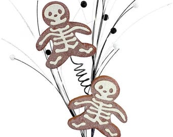 May include: Halloween-themed decorative stem featuring two gingerbread man-shaped ornaments with white skeleton designs. The ornaments are brown with white accents, attached to black and white sprigs with black and white decorative balls.