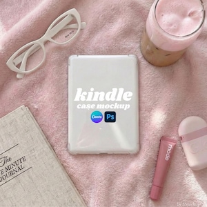 May include: A white Kindle case mockup with the text "kindle case mockup" and Canva and Photoshop logos. The image also includes white spectacles, a pink drink, a journal, and pink lip balm on a pink blanket.