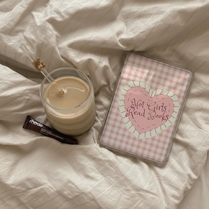May include: A glass of coffee with a straw and a small teddy bear decoration, a tube of rhode lip treatment, and a phone case with a pink gingham pattern and the text "Hot Girls Read Books."