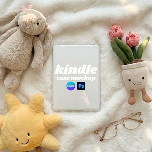 May include: A white Kindle case mockup with the text "kindle case mockup" and Canva and Photoshop logos. The case is surrounded by a plush bunny, a yellow star-shaped toy, a small potted plant with pink flowers, and gold-rimmed glasses.