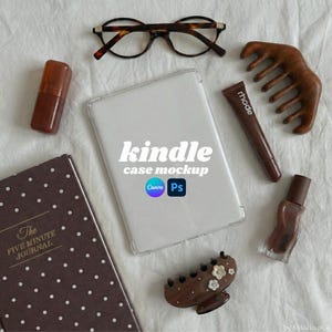 May include: A flat lay featuring a Kindle case mockup with the text "kindle case mockup". Other items include a brown journal, eyeglasses, a wooden comb, a tube of lip product, a bottle of nail polish, a hair clip, and a brown lipstick.