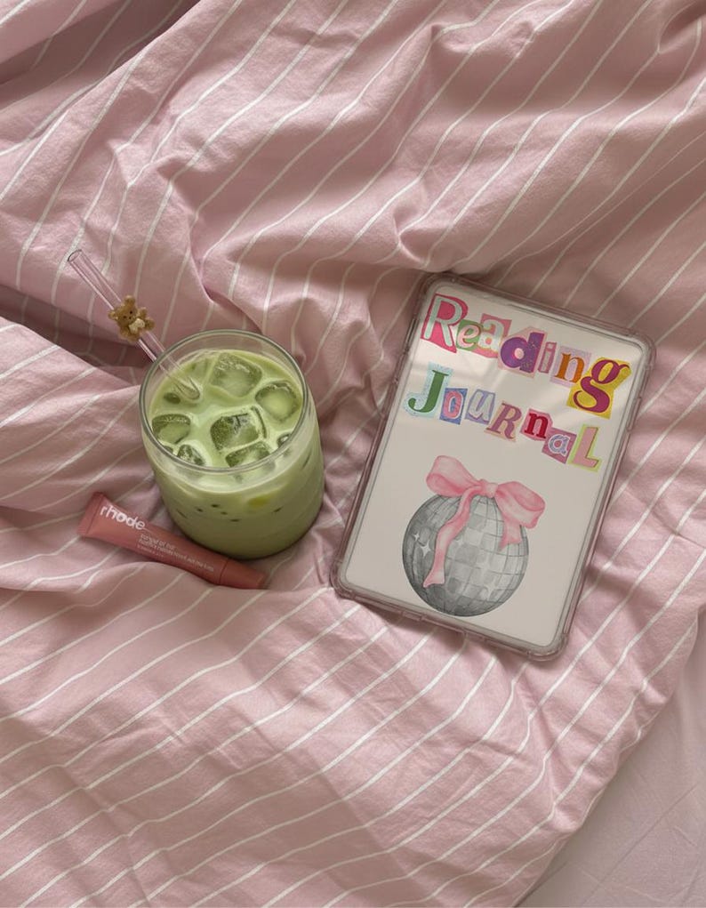 May include: A refreshing matcha latte with ice cubes in a clear glass, a lip product, and a "Reading Journal" with a disco ball illustration and pink bow, all on pink striped bedding.