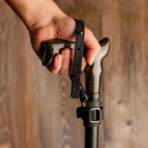 以下が含まれることがあります： 黒い金属製の先端と、金属製のバックルが付いた黒い革製のリストストラップが、木製のステッキに取り付けられています。ステッキは、茶色の木製のハンドルが付いています。