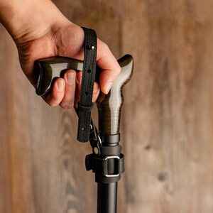 Puede incluir: Una vara de madera con un eje de metal negro, con una correa de cuero negro con una hebilla de metal.