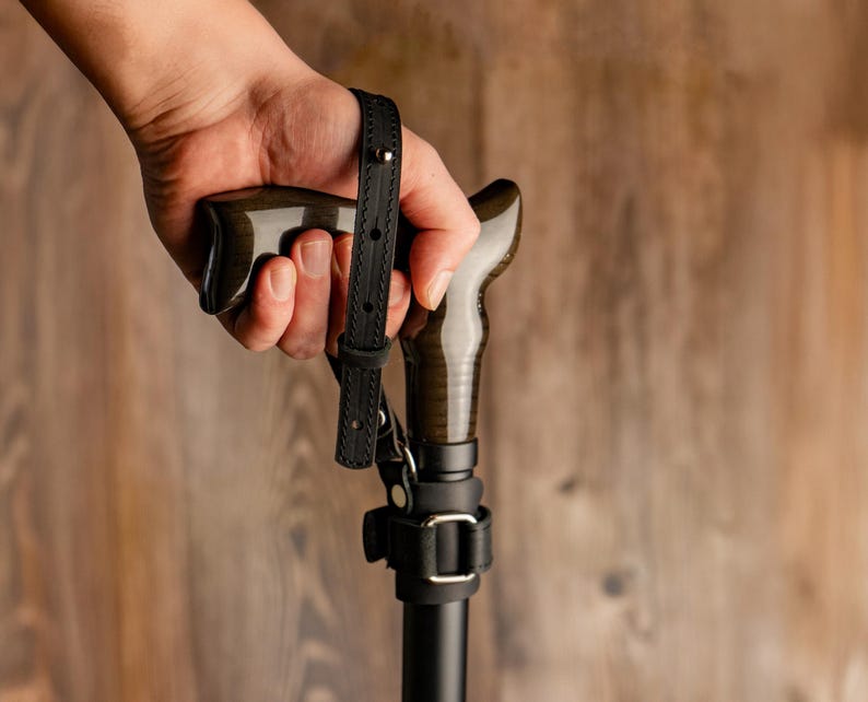 Puede incluir: Una vara de madera con un eje de metal negro, con una correa de cuero negro con una hebilla de metal.