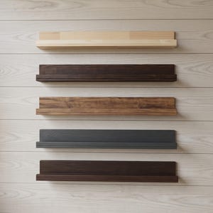 Op de afbeelding: Vijf horizontale, aan de muur gemonteerde zwevende planken, verticaal boven elkaar geplaatst. Elke plank heeft een plat achterpaneel en een smalle voorrand. De planken zijn afgewerkt in vijf verschillende houttinten: licht natuurlijk, donkerbruin, middenbruin, antracietgrijs en diep espresso.
