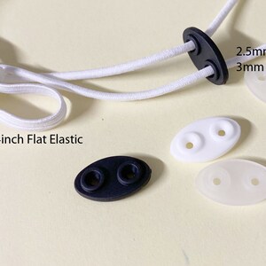 May include: White elastic cord with two white plastic slider toggles and one black plastic slider toggle. The elastic cord is labeled "1/4inch Flat Elastic". One of the white toggles is labeled "2.5mm Round Elastic or 3mm Round Elastic".