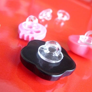 May include: Assortment of colorful buttons with different shapes and designs. The buttons are made of plastic and have a clear plastic loop for sewing. The buttons are in various colors, including pink, black, and white.