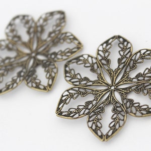 May include: Two ornate metal flower-shaped charms with a filigree design. The charms are made of a brass-colored metal and have a delicate, intricate pattern.