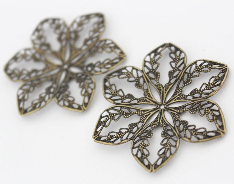 May include: Two ornate metal flower-shaped charms with a filigree design. The charms are made of a brass-colored metal and have a delicate, intricate pattern.