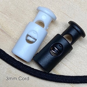 May include: Two plastic cord stoppers, one black and one white, designed for 3mm cord. The stoppers have a spring mechanism to secure the cord.