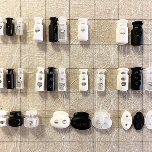 Peut inclure: Assortiment de fermoirs &agrave; bascule en plastique blanc et noir avec un m&eacute;canisme &agrave; ressort. Les fermoirs sont de diff&eacute;rentes tailles et styles, y compris des options &agrave; un et deux trous.