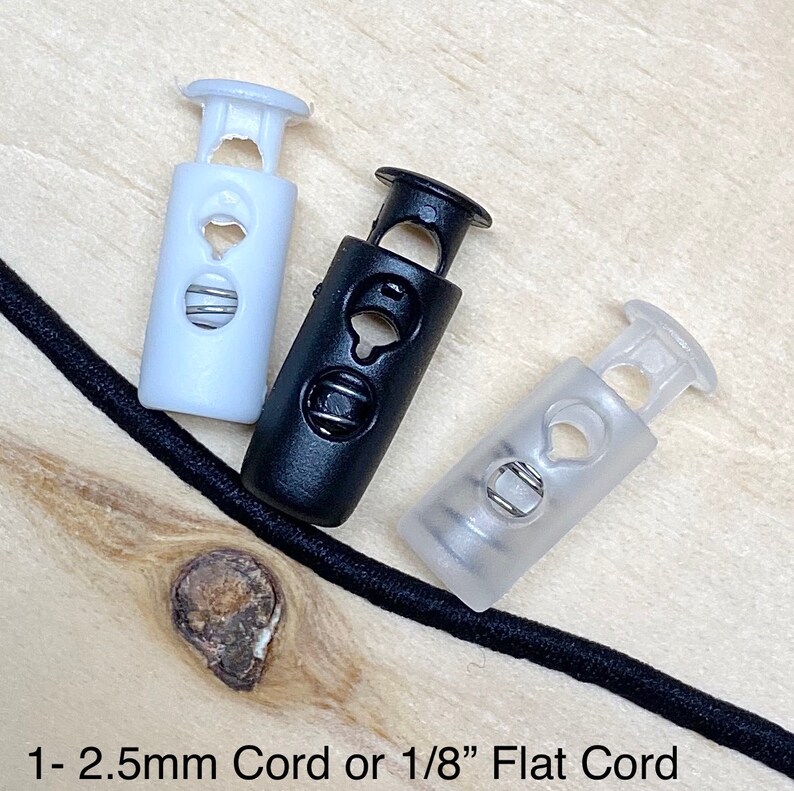 May include: Three cord stoppers in different colors: white, black, and clear. The stoppers are designed to secure cords or straps.