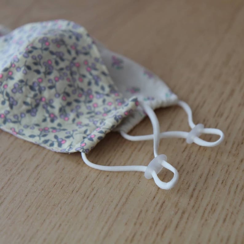 May include: A white face mask with a floral pattern and white elastic straps with plastic adjusters.