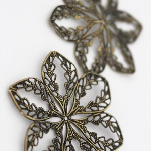 May include: Two ornate metal flower-shaped charms in a bronze finish. The charms have a delicate, intricate design with a cutout pattern.