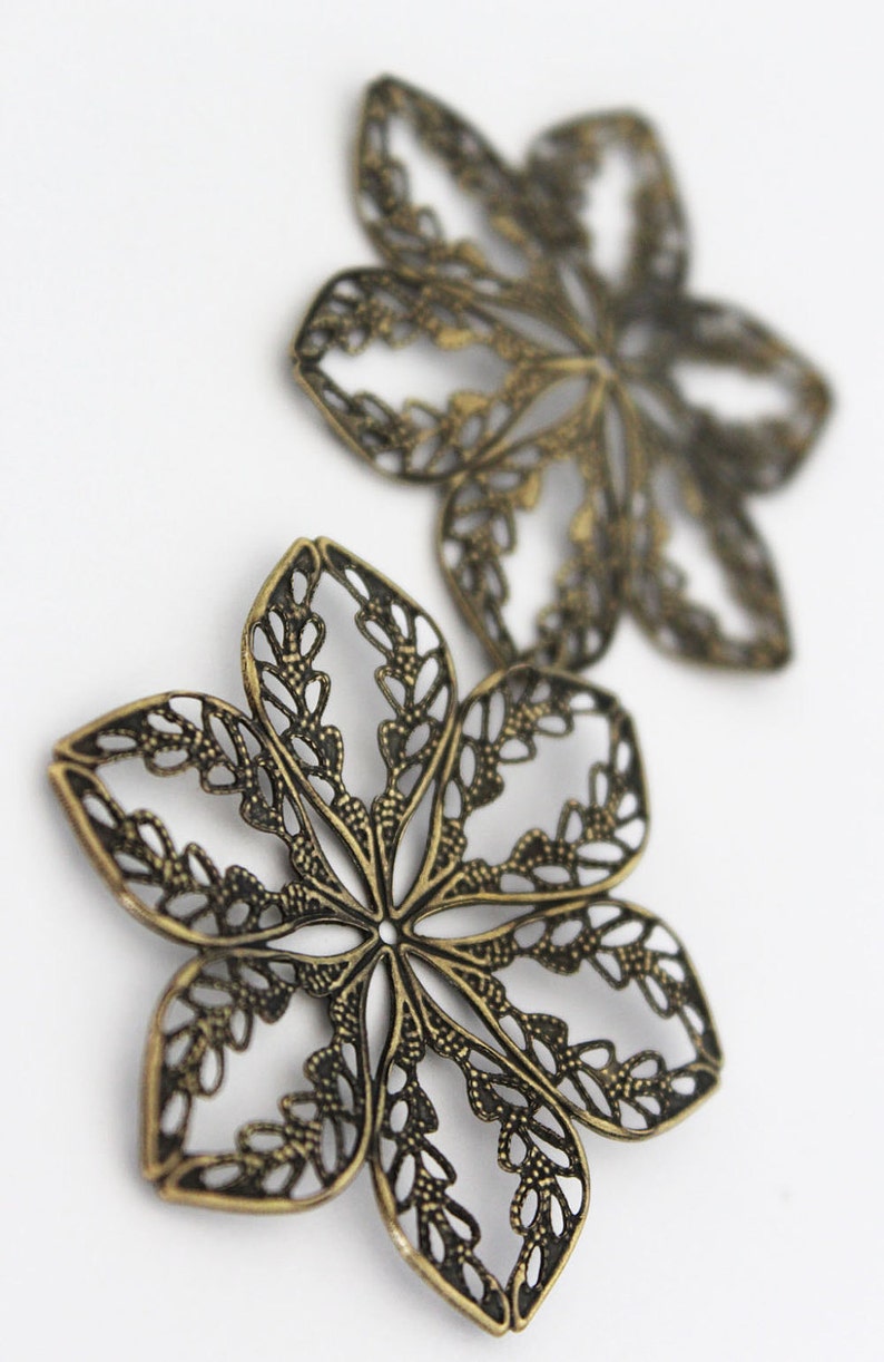 May include: Two ornate metal flower-shaped charms in a bronze finish. The charms have a delicate, intricate design with a cutout pattern.