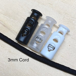 May include: Three cord stoppers, one black, one clear, and one white. The stoppers are designed to hold cords in place. The text "3mm Cord" is visible in the image.