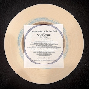 May include: A roll of beige double-sided adhesive tape by Sookwang, also known as Scor-Pal Tape. A square white label is centered on the roll, featuring black text detailing product specifications, safety certifications, and usage instructions.
