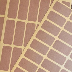 May include: Sheets of rectangular brown stickers with rounded corners, arranged on a light yellow backing. The stickers are evenly spaced and ready for use. Ideal for labeling or crafting projects.