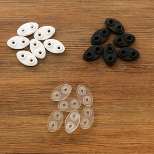 May include: Assortment of clear, white, and black plastic eyeglass nose pads. The nose pads are oval shaped with two small holes in each.