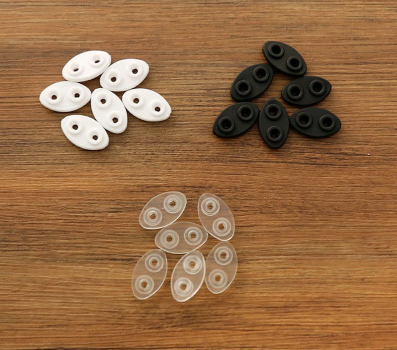 May include: Assortment of clear, white, and black plastic eyeglass nose pads. The nose pads are oval shaped with two small holes in each.