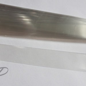 May include: A stack of clear plastic sleeves, with one sleeve laid out flat. The sleeves are approximately 10 inches long and 1 inch wide. The sleeves are ideal for protecting documents, photos, or other items.