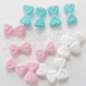 May include: Assortment of fabric bows in blue, pink, and white. The bows are small and have a textured surface.