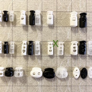 Peut inclure: Assortiment de fermoirs &agrave; bascule en plastique blanc et noir, certains avec des inserts en plastique transparent. Les fermoirs ont deux trous et sont utilis&eacute;s pour ajuster la longueur des cordons ou des sangles.