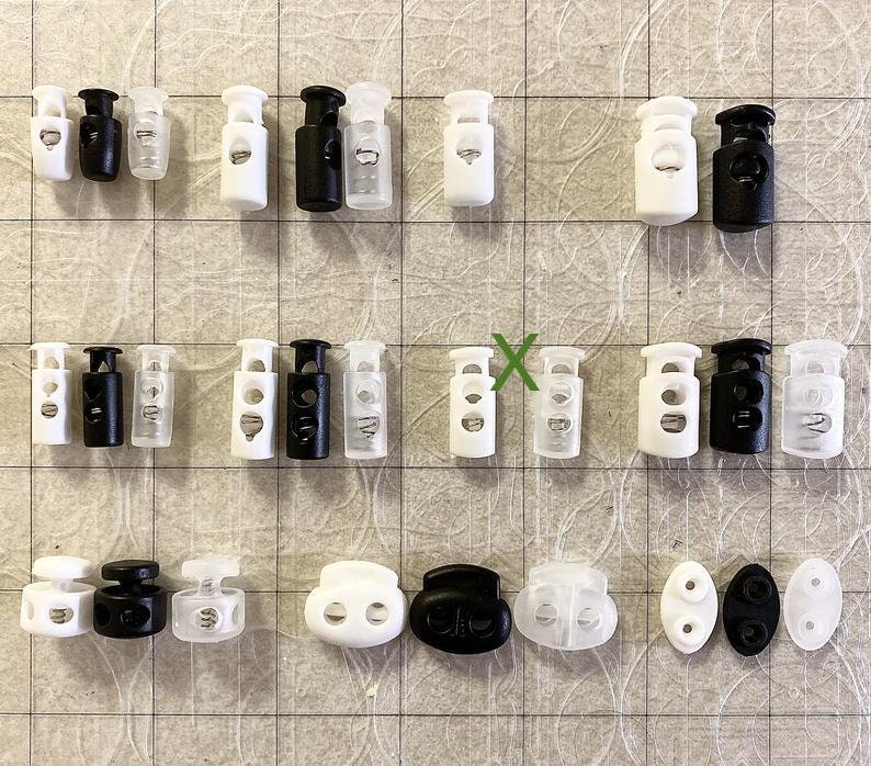 Peut inclure: Assortiment de fermoirs &agrave; bascule en plastique blanc et noir, certains avec des inserts en plastique transparent. Les fermoirs ont deux trous et sont utilis&eacute;s pour ajuster la longueur des cordons ou des sangles.