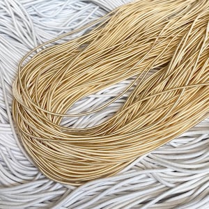 May include: A close-up of a pile of gold elastic cord, with a white elastic cord in the background.