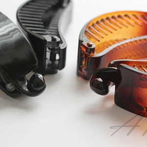 以下が含まれることがあります： 黒と茶色のプラスチック製のヘアクリップが2つずつ。クリップは半円形で、内側に歯が並んでいます。茶色のクリップには、裏側に「Boho Chic」という文字が印刷されています。