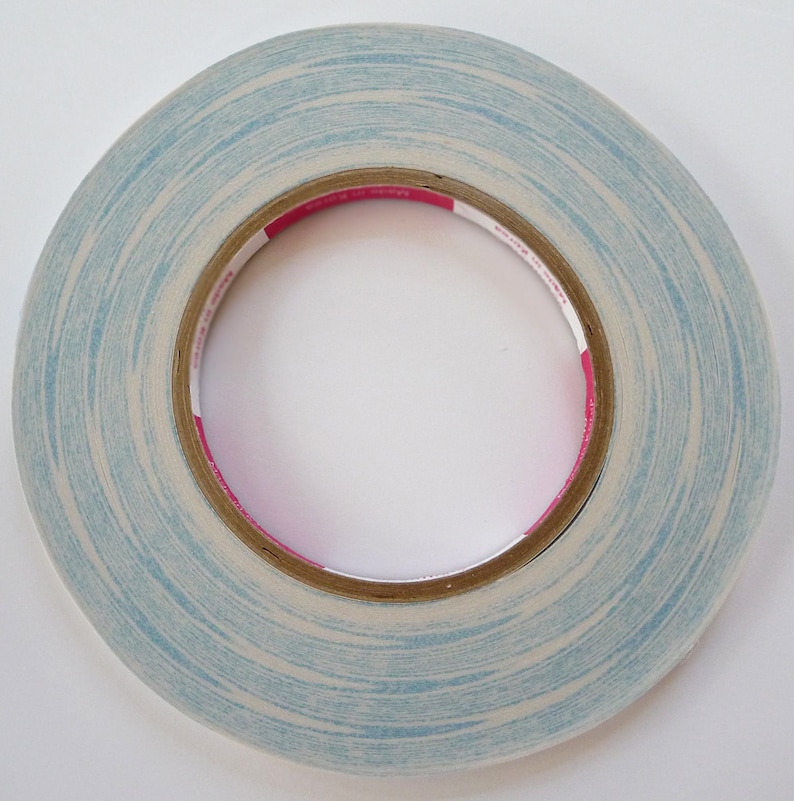 Pode incluir: Um rolo de fita adesiva de dupla face azul e branca com um r&oacute;tulo rosa. A fita est&aacute; sobre um fundo branco.