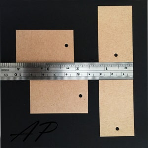 May include: Two brown paper gift tags with holes punched in the top. The larger tag is approximately 2 inches wide and 3 inches long. The smaller tag is approximately 1.5 inches wide and 2 inches long. The tags are on a black background.