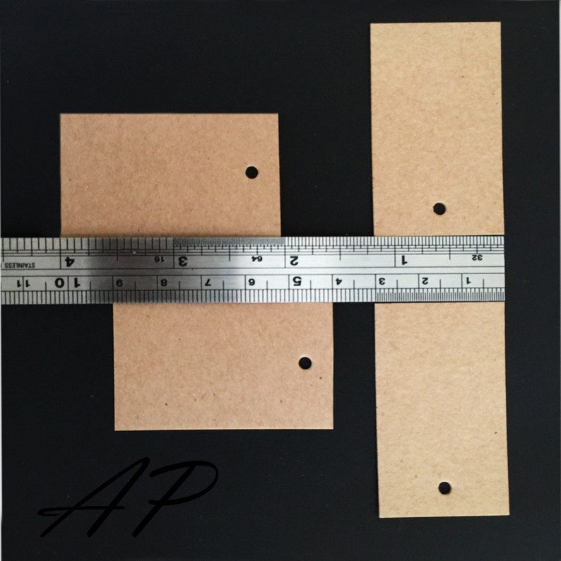 May include: Two brown paper gift tags with holes punched in the top. The larger tag is approximately 2 inches wide and 3 inches long. The smaller tag is approximately 1.5 inches wide and 2 inches long. The tags are on a black background.