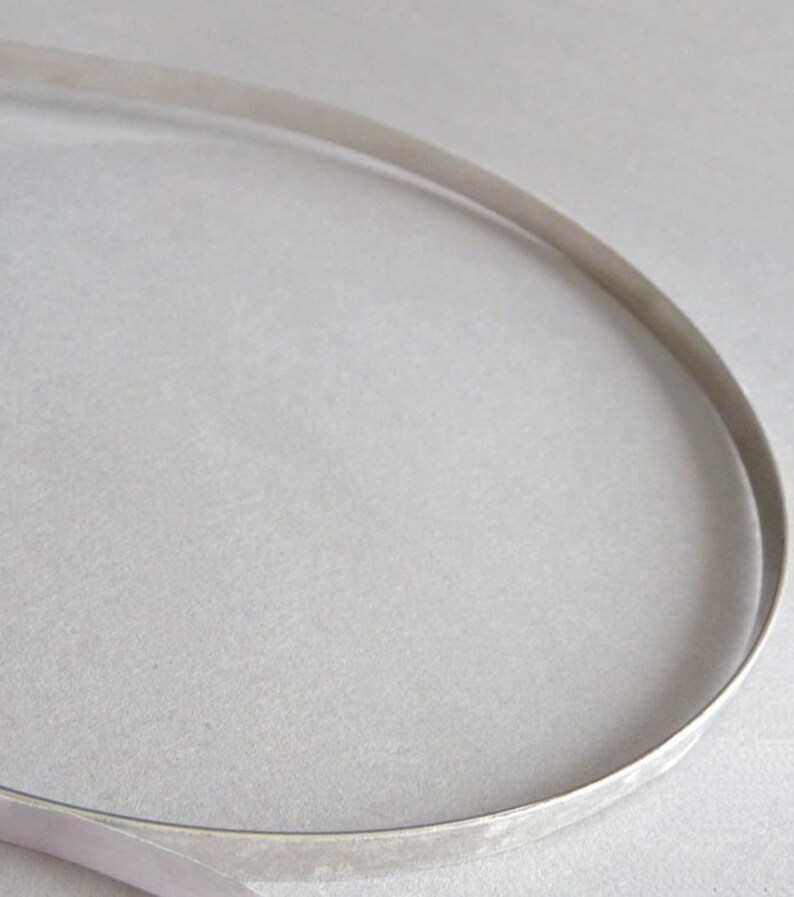 May include: A thin, flexible, silver-colored metal strip curved into a partial oval shape. The material has a smooth, reflective surface with a consistent width throughout its length, forming a simple, open-ended loop structure.