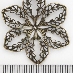 May include: A bronze-colored metal flower charm with a delicate, intricate design. The charm is approximately 2 inches in diameter and has a hole in the center for attaching to jewelry or other crafts.
