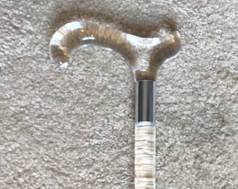 May include: A clear acrylic walking stick with a silver metal accent and a curved handle.