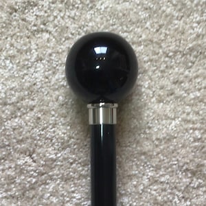 May include: A black walking stick with a round, black, polished knob on top.
