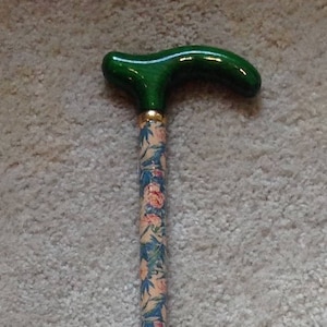 May include: A green and floral patterned walking stick with a curved handle. The handle is a bright green color and the stick is decorated with a floral pattern in shades of pink, blue, and green.
