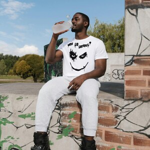 May include: A white t-shirt with a black graphic of a smiling face and the text "Why So Serious?". The person is wearing gray sweatpants and black rollerblades. A clear water bottle is being held up to the person's mouth.