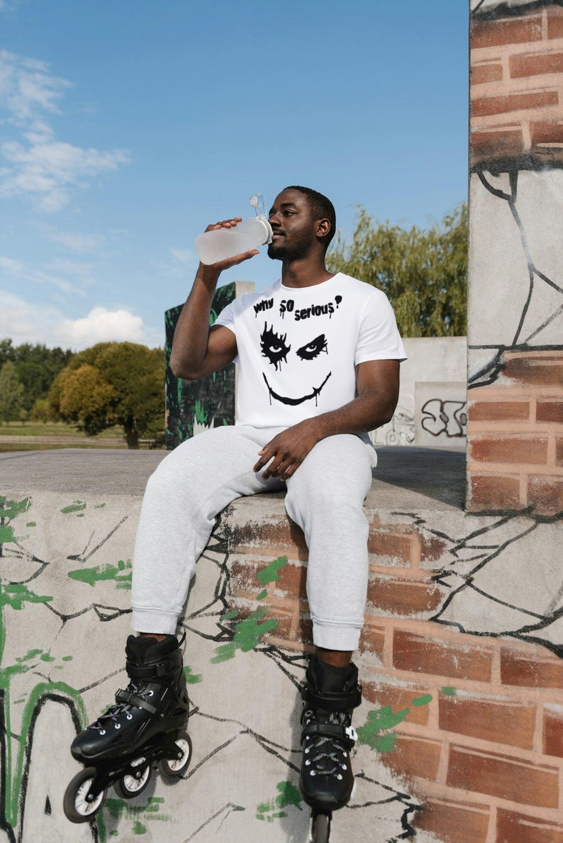 May include: A white t-shirt with a black graphic of a smiling face and the text "Why So Serious?". The person is wearing gray sweatpants and black rollerblades. A clear water bottle is being held up to the person's mouth.
