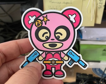 May include: Pink bear sticker with a white X on each ear, holding two blue toy guns. The bear has a yellow smiley face on its forehead and a yellow belt with a gold buckle.