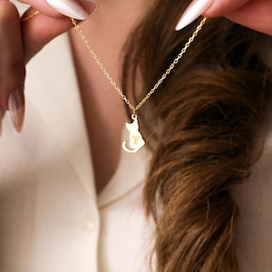 May include: A gold necklace with a cat-shaped pendant. The pendant has a small letter 'P' engraved on it.