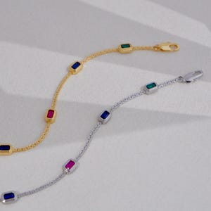 Puede incluir: Dos pulseras delicadas. Una es dorada, la otra plateada. Cada una presenta piedras preciosas rectangulares y coloridas: azul, rojo y verde. La pulsera dorada tiene un cierre de mosquetón. La pulsera plateada también tiene un cierre de mosquetón.